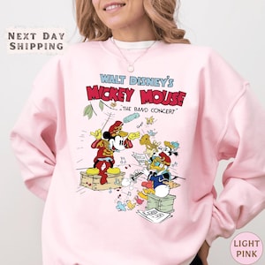 A woman wearing a pink sweatshirt with a Disney Mickey Mouse graphic and text.