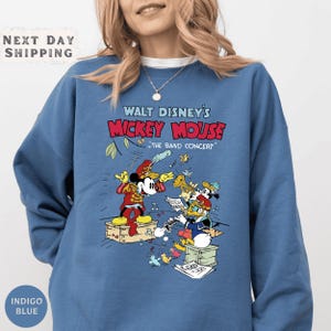 A woman wearing a blue sweatshirt with a graphic of Mickey Mouse and other Disney characters from Walt Disney's Mickey Mouse concerts.