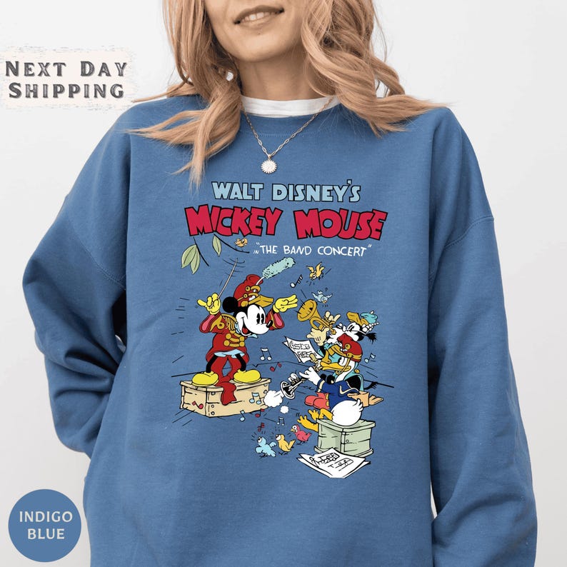 A woman wearing a blue sweatshirt with a graphic of Mickey Mouse and other Disney characters from Walt Disney's Mickey Mouse concerts.