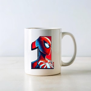 Pu&ograve; includere: Tazza in ceramica bianca con un'illustrazione di Spiderman rossa e blu e il numero "1" stampato su di essa.