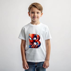 Pu&ograve; includere: Una maglietta bianca con una grafica di Spiderman rossa e blu sul davanti. La grafica mostra Spiderman che sbircia da dietro la lettera "B".