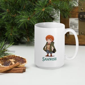 May include: White ceramic mug featuring a cartoon illustration of a character with red hair, wearing a green cloak and brown boots. The word "SAMWISE" is printed in green below the character.