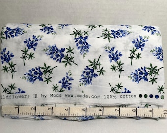 May include: White cotton fabric with a blue and green floral print of bluebonnets. The fabric has the text "Wildflowers III by Moda www.moda.com 100% cotton" printed on the bottom edge.