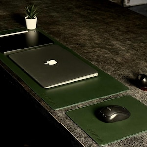 Op de afbeelding: Een donkergroene bureau-opstelling met een laptop, tablet en muis op bijpassende groene bureaumatten. Een kleine potplant en een pijp zijn ook aanwezig. De bureaumatten hebben de naam "SOPHIA" erop gedrukt.