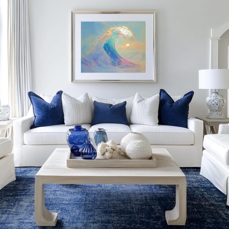 Puede incluir: Un sof&aacute; blanco con almohadas azules y una mesa de caf&eacute; blanca con art&iacute;culos decorativos azules y blancos. El sof&aacute; est&aacute; frente a una pared blanca con una pintura enmarcada de una ola azul.