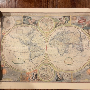 May include: An antique world map printed on paper with a vintage aesthetic. The map is divided into two hemispheres, with the Americas on the left and Europe, Asia, and Africa on the right. The map is surrounded by decorative borders and includes illustrations of celestial bodies and mythical creatures.