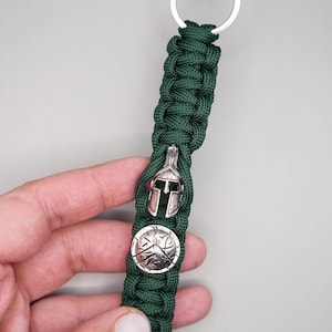 May include: A dark green paracord keychain with a silver Spartan helmet and shield charm.