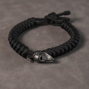 May include: A black paracord bracelet with a silver metal helmet charm.