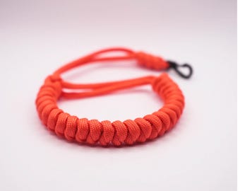 May include: A bright orange paracord bracelet with a black metal clasp.