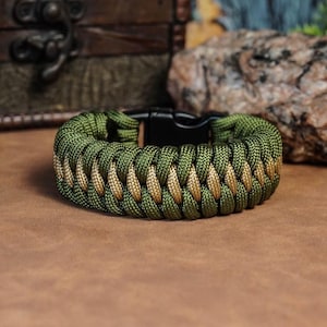 May include: A green and tan paracord bracelet with a black buckle closure. The bracelet is made of woven paracord and has a camouflage pattern.