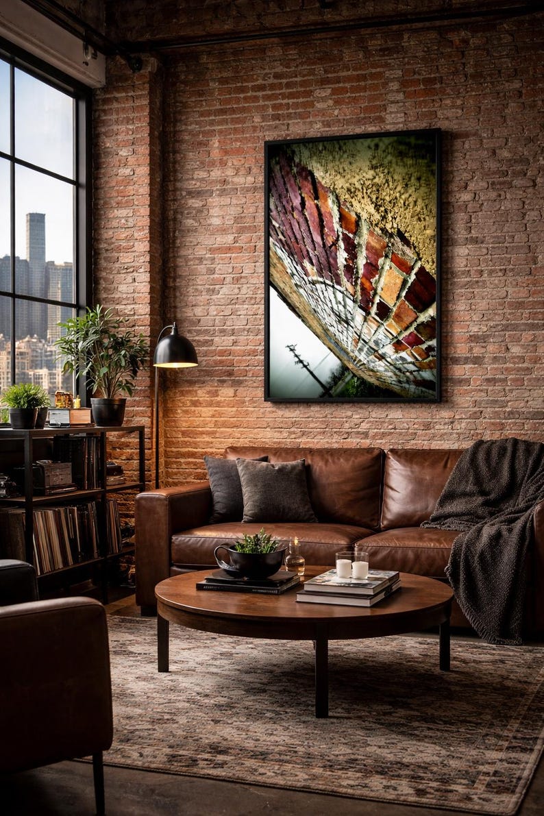 a cozy living room with a brick wall, a large window overlooking a city skyline, and a brown leather couch. A wooden coffee table sits in front of the couch, and a framed artwork of a colorful butterfly is hanging on the wall above it.