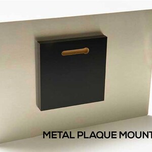 a black square plaque mounted on a white wall using a metal plate.