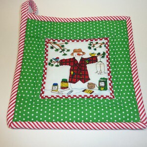 May include: A square, quilted potholder with a green polka dot pattern and red and white striped trim. The center features a snowman illustration in a plaid jacket, holding a bird feeder. The potholder has a loop for hanging.