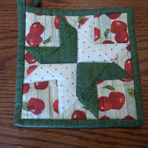 May include: A green and white quilted pot holder with a red apple and white polka dot design.