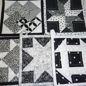 May include: Set of five black and white quilted pot holders with different geometric patterns. The pot holders have a black border and a loop for hanging.