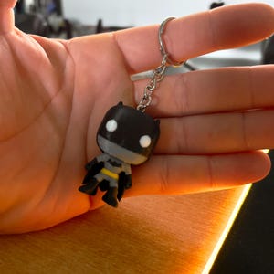 Op de afbeelding: Een zwarte en grijze Batman-figuur sleutelhanger met een zilveren ketting en ring. De sleutelhanger is gemaakt van plastic en heeft een 3D-ontwerp.