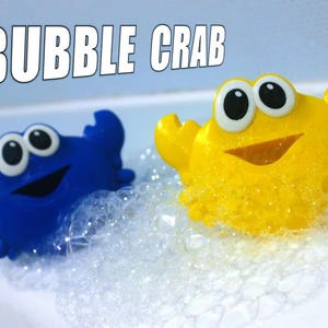 Può includere: Due giocattoli da bagno a forma di granchio, uno blu e uno giallo, sono in una vasca di bolle. Il granchio blu ha un viso sorridente e occhi grandi. Il granchio giallo ha un viso sorridente e occhi grandi. Il testo "BUBBLE CRAB" è scritto in lettere bianche su uno sfondo blu nella parte superiore dell'immagine.