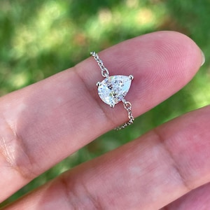 May include: A delicate silver chain bracelet featuring a pear-shaped, clear gemstone. The gemstone is set in a silver prong setting and is the focal point of the bracelet. The chain is fine and adds a touch of elegance.