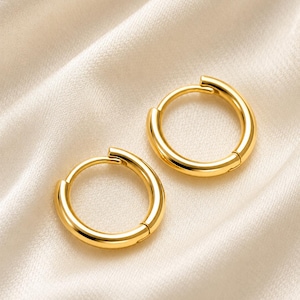 May include: A pair of polished gold hoop earrings with a smooth, circular design. Each earring features a hinged closure mechanism, creating a seamless and continuous loop appearance. The metal has a bright, reflective finish with a warm yellow tone.