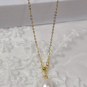 May include: A delicate gold-colored necklace featuring a lustrous, teardrop-shaped pearl pendant. The chain is fine and elegant, with a small gold bead accent. The necklace is displayed against a soft, white background, highlighting its simple beauty.