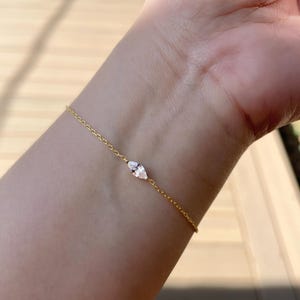 Pu&ograve; includere: Un delicato braccialetto d'oro con una gemma taglio marquise. Il braccialetto &egrave; una catena sottile con una gemma centrale, allungata e trasparente. Il gioiello &egrave; esposto su un polso, mostrando l'elegante design del braccialetto.