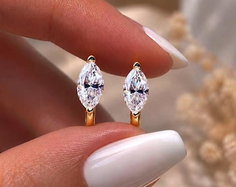 Op de afbeelding: Een paar gouden oorringen, elk voorzien van een enkele heldere edelsteen in marquise-slijpvorm. De gefacetteerde stenen zijn verticaal gezet in een gepolijst gouden metalen frame, wat zorgt voor een heldere en reflecterende uitstraling.