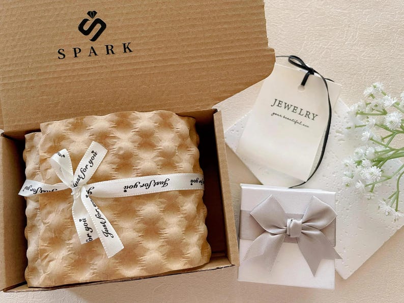 Pu&ograve; includere: Una confezione regalo con la scritta "SPARK" e il logo, contenente un articolo avvolto legato con un nastro con la scritta "Just for you". Una piccola scatola bianca con un fiocco grigio e un'etichetta con la scritta "JEWELRY".