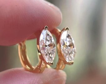May include: A pair of gold hoop earrings, each featuring a single marquise-cut clear gemstone set in a polished gold frame. The earrings are designed as small hoops with a hinged closure, showcasing a bright, reflective finish on the metal.