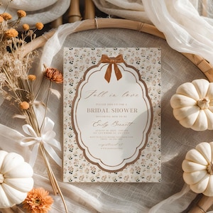 May include: A rectangular bridal shower invitation card featuring a floral pattern with small orange and green flowers. The center has a white scalloped frame with a brown bow at the top. Text reads: Fall in love, Please join us for a bridal shower, honoring mom to be, Emily Bennett, August 10, 2025, 3:00 PM, 123 anywhere st, any city, RSVP to Quita before November 25th, phone 123 456 7890, registered at www.martylo.com.