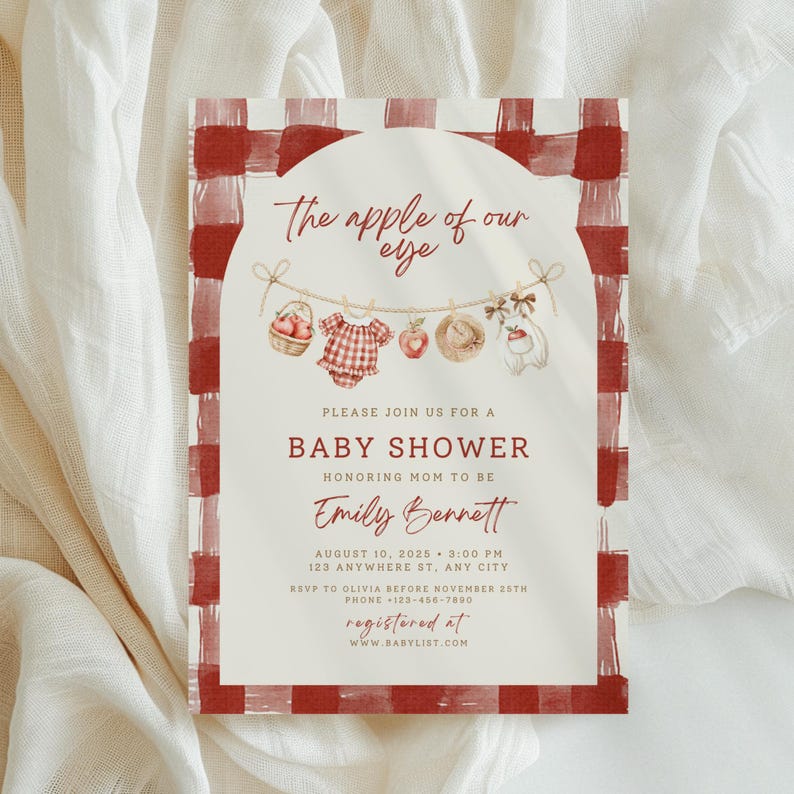 Pu&ograve; includere: Un invito rettangolare per baby shower con bordo a quadri rossi e bianchi e pannello centrale ad arco. Il testo recita: The apple of our eye, Please join us for a baby shower honoring mom to be Emily Bennett, August 10, 2025, 3:00 PM, 123 Anywhere St, Any City, RSVP to Olivia before November 25th, Phone +123-456-7890, Registered at www.babylist.com. Illustrazioni di un cesto di mele, un body a quadri, una mela, un cappello di paglia e un orsacchiotto sono appesi a una corda.