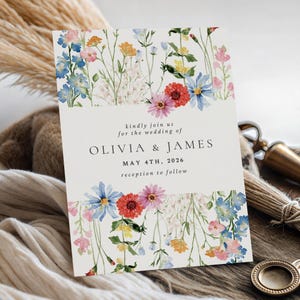 May include: A wedding invitation with a floral design. The invitation features a cream-colored background with colorful watercolor flowers in shades of blue, pink, red, and yellow. The text reads "kindly join us for the wedding of OLIVIA & JAMES MAY 4TH, 2026 reception to follow."