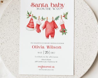 May include: A white invitation card with red text and watercolor illustrations. The text reads "Santa baby is on the way!" and invites guests to a baby shower for Olivia Wilson on December 25th. The card features baby clothes and stockings.