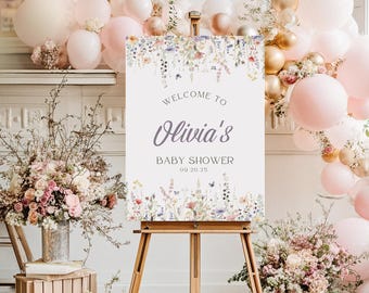 Puede incluir: Un caballete de madera exhibe un letrero que dice "Welcome to Olivia's Baby Shower 09.20.25." El letrero tiene un borde floral con flores rosas, moradas y amarillas. El fondo incluye globos rosas y dorados y arreglos florales.
