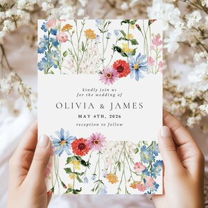 May include: A rectangular wedding invitation card featuring watercolor illustrations of colorful wildflowers at the top and bottom. The text reads: kindly join us for the wedding of OLIVIA & JAMES MAY 4TH, 2026 reception to follow.