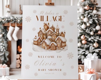 May include: A white sign on an easel with the text "It takes a VILLAGE" and "WELCOME TO Olivia's BABY SHOWER". The sign features a watercolor illustration of a snow-covered village with snowflakes. The background includes a Christmas tree and gifts.