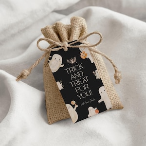 K&ouml;nnte beinhalten: Ein kleiner Jutesack, der mit Bindfaden gebunden ist und ein schwarzes Etikett mit Halloween-Illustrationen aufweist. Auf dem Etikett steht "Trick and Treat for You!" mit Geister- und K&uuml;rbisgrafiken. Der Beutel ist mit Leckereien gef&uuml;llt.