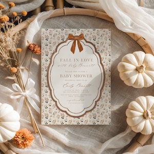 Puede incluir: Una tarjeta de invitación rectangular para baby shower con estampado floral, un marco festoneado central y un gráfico de lazo marrón. El texto dice: FALL IN LOVE with baby Bennett, PLEASE JOIN US FOR A BABY SHOWER, Emily Bennett, AUGUST 10, 2025, 3:00 PM.