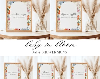 Puede incluir: Carteles de baby shower con bordes florales y marcos de madera. Los carteles incluyen textos como "custom sign", "diaper raffle", "favors" y "mimosa bar". La frase "baby in bloom" también está presente.