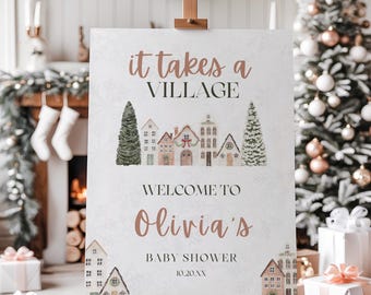 May include: A white sign on a wooden easel with the text "It takes a VILLAGE" in rose gold. Below, it reads "WELCOME TO Olivia's BABY SHOWER". The sign features watercolor illustrations of houses and trees, with the date 10.20.XX.