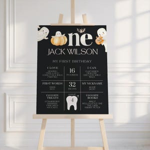 K&ouml;nnte beinhalten: Eine schwarz-wei&szlig;e Geburtstagstafel zum Thema Halloween auf einer Staffelei. Auf dem Schild steht "one" mit dem Namen "Jack Wilson" und "My First Birthday". Es enth&auml;lt Details wie Gewicht (7,26 kg), Gr&ouml;&szlig;e (81,28 cm) und Lieblingsdinge.