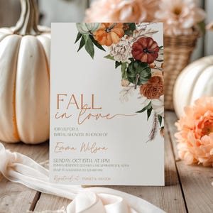 May include: A bridal shower invitation with the text "Fall in Love" in a stylish font. The invitation features a floral design with pumpkins and autumn colors. The invitation includes the date, time, and location.