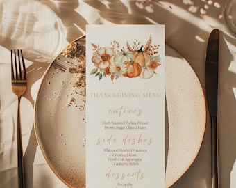 Könnte beinhalten: Thanksgiving-Menükarte mit floralen und Kürbis-Illustrationen. Das Menü listet Vorspeisen, Beilagen und Desserts auf. Die Karte liegt auf einem Teller mit Gabel und Messer, was eine festliche Tischdekoration ergibt.
