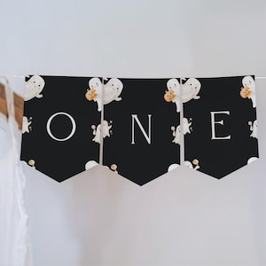 K&ouml;nnte beinhalten: Ein schwarzes Banner mit dem Wort "ONE" in wei&szlig;en Buchstaben. Das Banner ist mit Cartoon-Geistern dekoriert, die K&uuml;rbisse halten. Das Banner ist an einer wei&szlig;en Schnur befestigt, ideal f&uuml;r Halloween oder den ersten Geburtstag.