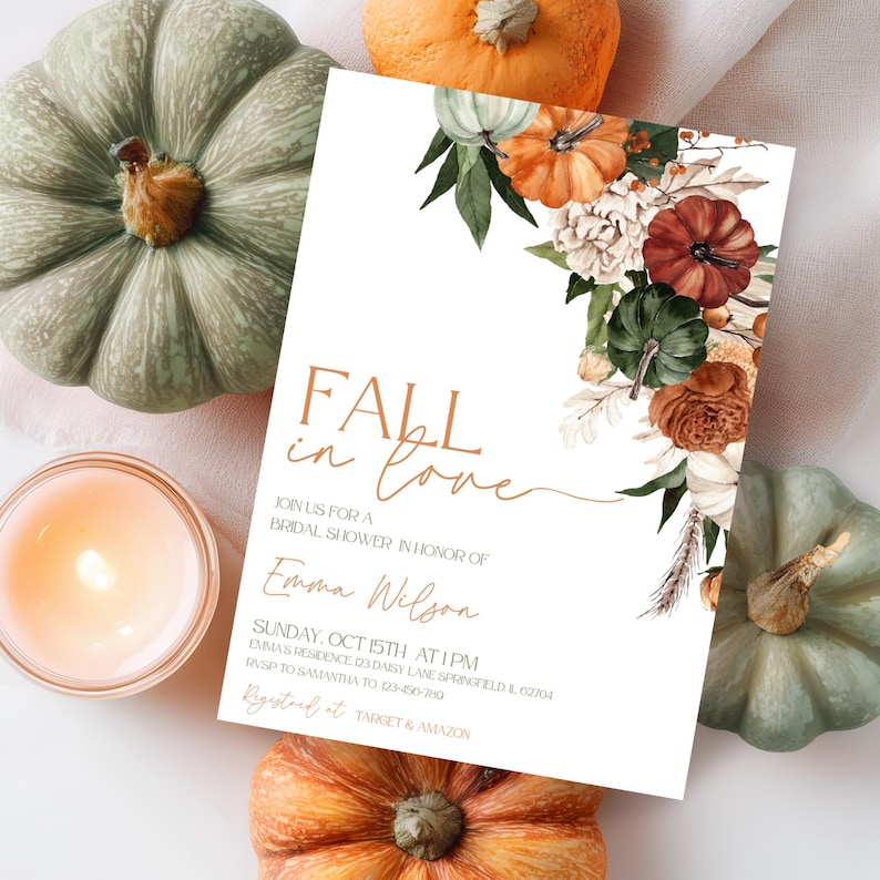 May include: A bridal shower invitation with the text "Fall in Love" and floral and pumpkin accents. The invitation is surrounded by pumpkins and a lit candle, creating a fall theme.