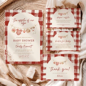 Pu&ograve; includere: Un set di cancelleria per baby shower con bordo a quadri rossi e bianchi e centro color crema. Le carte includono illustrazioni di un cestino, un body, una mela, un cappello e un coniglio appesi, con il testo The apple of our eye.