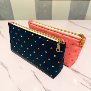 May include: Two zippered pouches with heart patterns. One pouch is navy blue with white and orange hearts, the other is pink with white hearts.