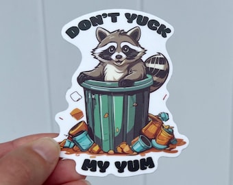 May include: A white sticker with a cartoon raccoon in a green trash can. The raccoon is looking up and has a mischievous expression. The text "Don't Yuck My Yum" is printed on the sticker.