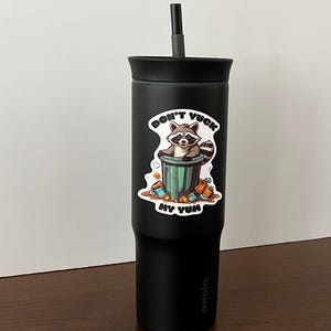 Sticker on black tumbler. Sticker pictures cute raccoon in trash can with the words "Don't Yuck My Yum".