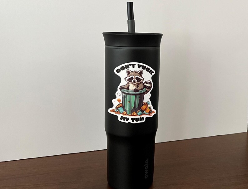 Sticker on black tumbler. Sticker pictures cute raccoon in trash can with the words "Don't Yuck My Yum".