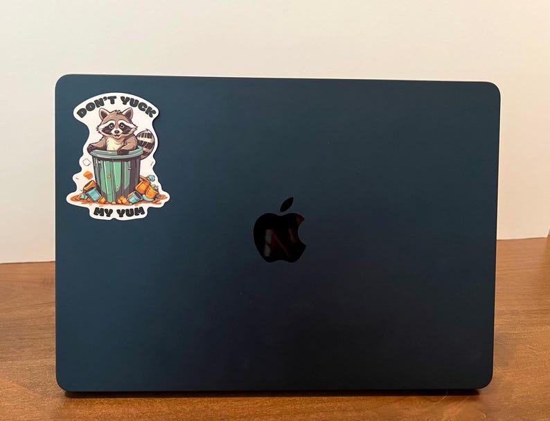 Sticker on black Apple laptop. Sticker pictures cute raccoon in trash can with the words "Don't Yuck My Yum".